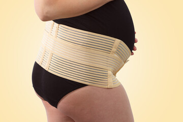 Pregnant woman with elastic maternity band on yellow background