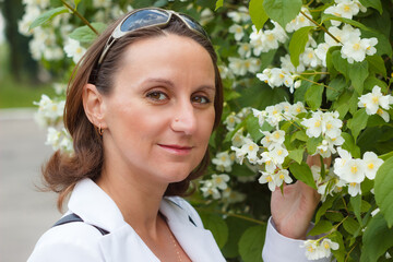 Beautiful caucasian woman near a jasmine bush. Young woman sniffs white flowers