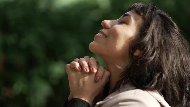 Hopeful woman praying to God standing outside looking at sky. Girl closing eyes in meditation. Contemplative person opening eye having HOPE