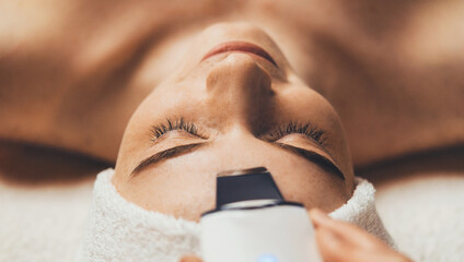 Portrait of woman face with closed eyes getting ultrasonic peeling in spa salon. Skin care. Girl...