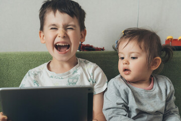 Two caucasian kids watching cartoons on tablet computer and laughing. Internet technology. Having fun