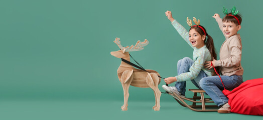 Funny little children with sledge and wooden reindeer on green background with space for text