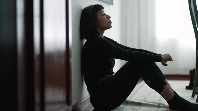 One pensive sad hispanic woman sitting at home floor pondering problems
