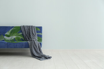 Comfortable sofa with print of monstera leaves near light wall in room