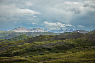 rolling tundra hills with distant sunny mountains and cloudy sky