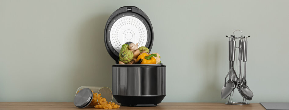 Modern multi cooker with vegetables on kitchen table