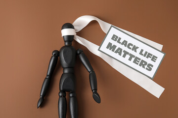 Black mannequin with white ribbon and paper sheet with text BLACK LIFE MATTERS on color background