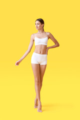 Young tanned woman in underwear on yellow background