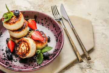 Plate with cottage cheese pancakes and cutlery on light background