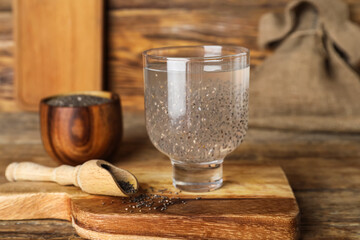 Glass with water and chia seeds on board against wooden background