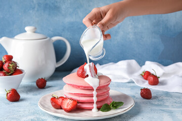 Woman pouring sauce onto tasty pink pancakes on color background
