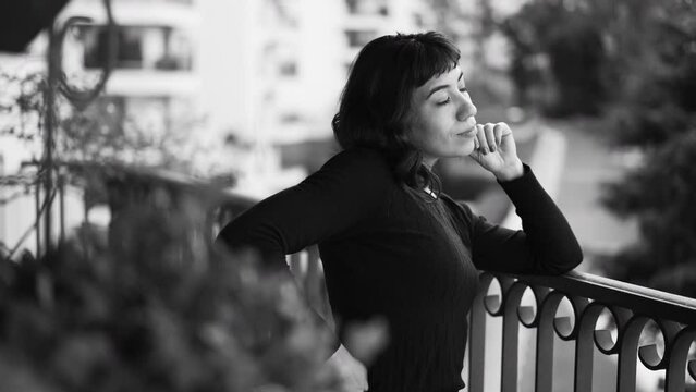 Pensive woman standing at balcony apartment in monochromatic black and white photo