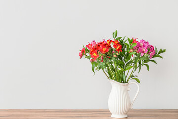 Vase with beautiful alstroemeria flowers on wooden tabletop near light wall