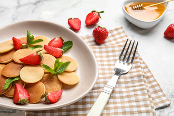 Plate of tasty mini pancakes with strawberry on light background, closeup