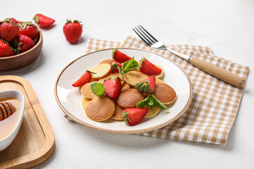 Plate with mini pancakes and delicious strawberry on light table