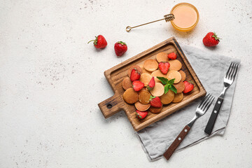 Wooden board with mini pancakes, delicious strawberry and honey on light background
