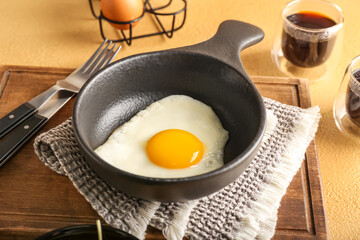 Wooden board with frying pan of fried egg on table, closeup