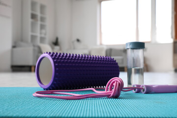 Foam roller with skipping rope and bottle of water on mat in living room