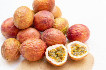 Delicious whole passion fruit shown here on a white background with one sliced in half exposing the pulp inside.