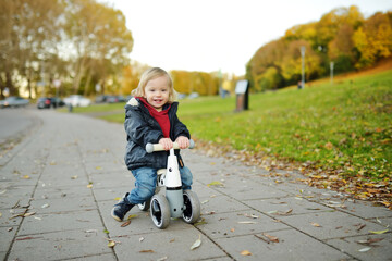 Funny toddler boy riding a baby scooter outdoors on autumn day. Kid training balance on mini bike...