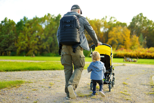 Young father walking in autumn park with toddler son in pushchair. Man pushing a stroller for toddler boy.