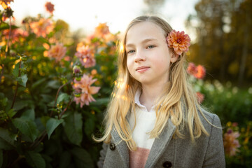 Naklejka premium Beautiful preteen girl in blossoming dahlia field. Child picking fresh flowers in dahlia meadow on autumn day.