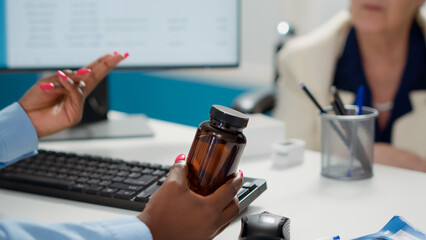 Female physician holding bottle of pills to give prescription treatment to old woman in wheelchair. Doctor giving medicine and drugs to patient with physical disability. Close up.