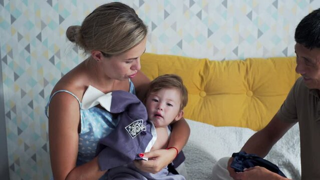 Caucasian mother and korean father are dressing up their son who is being naughty in traditional korean costume preparing him for etiquette at his first birth day. Loving family at home