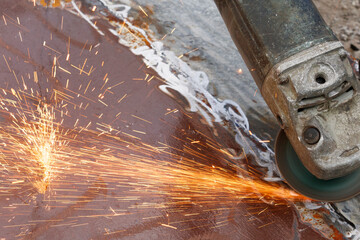 A man is polishing metal. The master works on a grinding machine. Leveling material. Sparks fly from under the grinder.