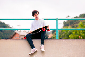Young man sitting on a skateboard ramp and holding his skateboard. Young man having fun outdoors. © Marcio
