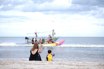 Mother and son waved greetings to father playing boat with friends.