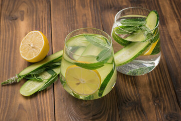 Two glasses with drinks of mint and cucumber with lemon on a wooden table.