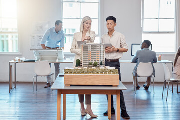 Confident business professionals in the field of architecture working together on building designs in a modern office. Team of male and female architects talk over a model construction for a project.