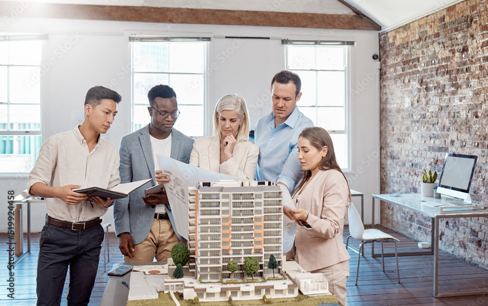 Poster A diverse team of architects working on a building model together inside the office. A group of engineers planning a reconstruction or design project of an apartment block with blueprint documents