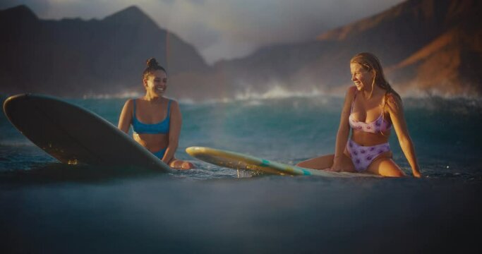 Girls surfing at sunset in Hawaii, smiling and waiting for the next wave