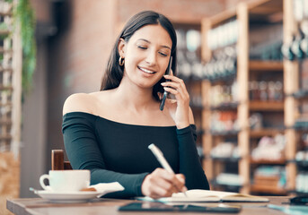 Beautiful, young and friendly woman talking on the phone and writing in a dairy at a coffee shop. Confident freelancer booking appointments and smiling on call in a restaurant on a summer weekend