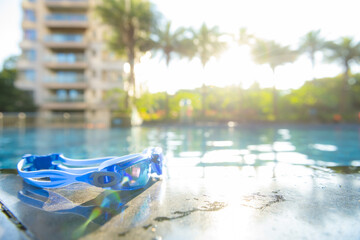 swimming goggles on the side of a swimming pool in a morning with a rising sun at horizontal composition