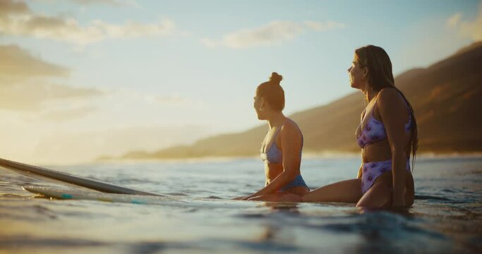 Beautiful surfer girls relaxing and enjoying golden sunset on the water waiting for the next wave, surfing in Hawaii