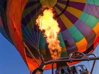 Hot air balloon burner flame fires into canopy as balloon floats through sky.