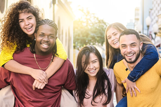 Multiracial young people walk happily in the city streets on piggyback rides - Guys and girls having fun together - Lifestyle concept - Selective focus