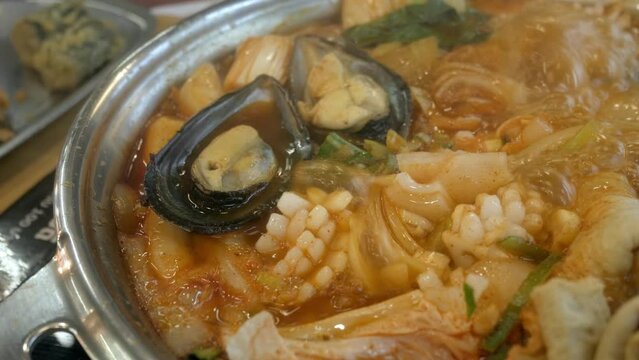 close up to boiling Korean Kimchi tteok pokki soup full with pork,squid,mussles,ehmook fish plate and vegetable. Asain korean traditional food