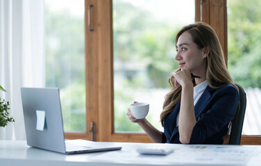 Beautiful young Asian businesswoman drinking a coffee working on laptop at office.