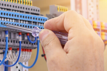 An electrical engineer installs modules in the control panel with a screwdriver.Sunflare.