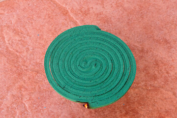 A burning anti-mosquito coil on a stand outdoors and smoke