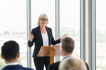 Naklejka na ściany i meble Senior business woman talking at podium speaker. Senior business woman wear suit standing discussing business strategy plan at podium in business conference room