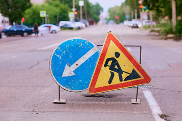 A metal frame with worn, scratched road works and bypass road signs closes a hole in the asphalt of...