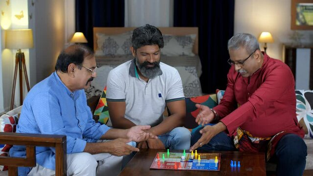 Three middle-aged Indian men in their late forties playing a board game - rolling the dice  childhood memories  loud laugh  happy time. Three old friends spending quality time in fun activities - o...