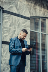 Smiling european businessman in suit with laptop talking phone near office building during break.A handsome guy with a black beard.