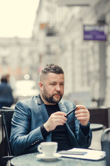 A man is holding a pen in his hands, thinking. A guy is drinking coffee in a cafe.