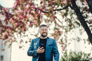 Portrait of handsome successful smiling man near tree in park.Cheerful man with a phone in his hands.